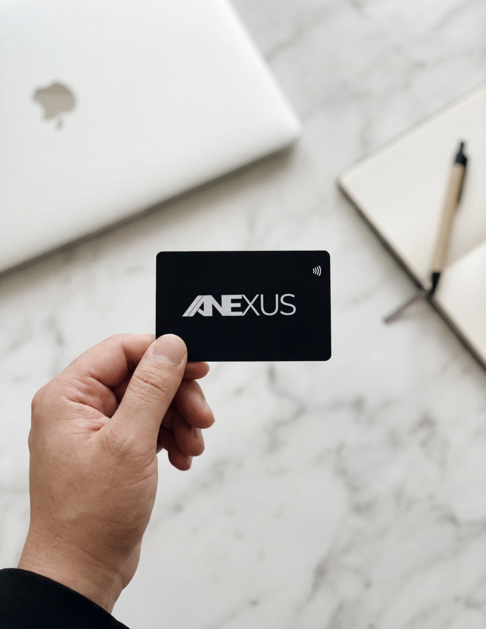 Une carte de visite NFC Anexus en métal noir tenue à la main, symbole sans contact visible